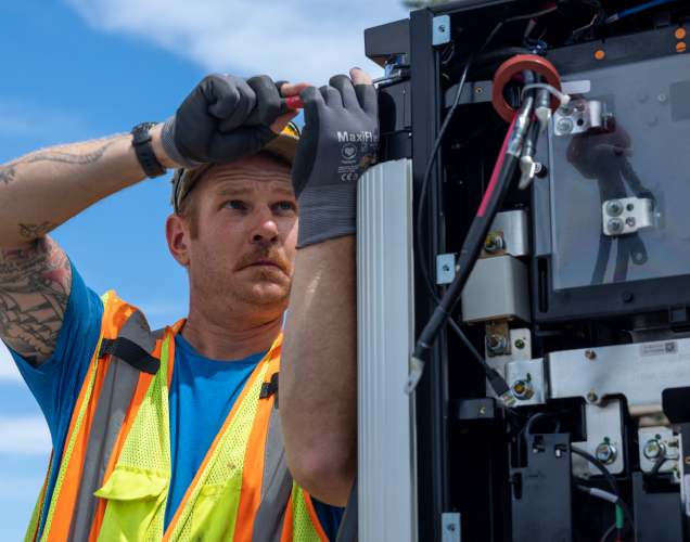 A worker in a neon safety vest and gloves performing maintenance on a ChargePoint Express Plus.