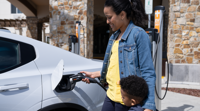 Mother with child charging an electric vehicle at a public charging station.