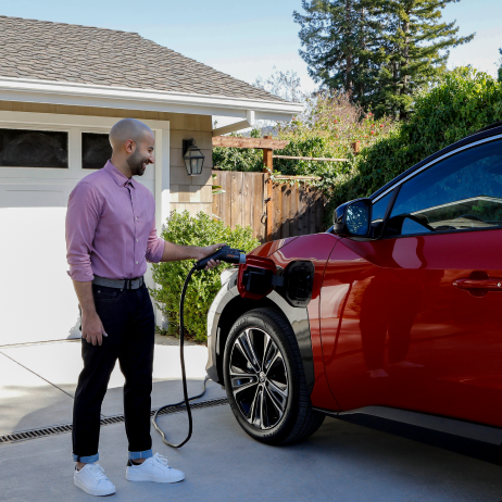 Man plugging in ChargePoint EV charger to charge red car in residential driveway